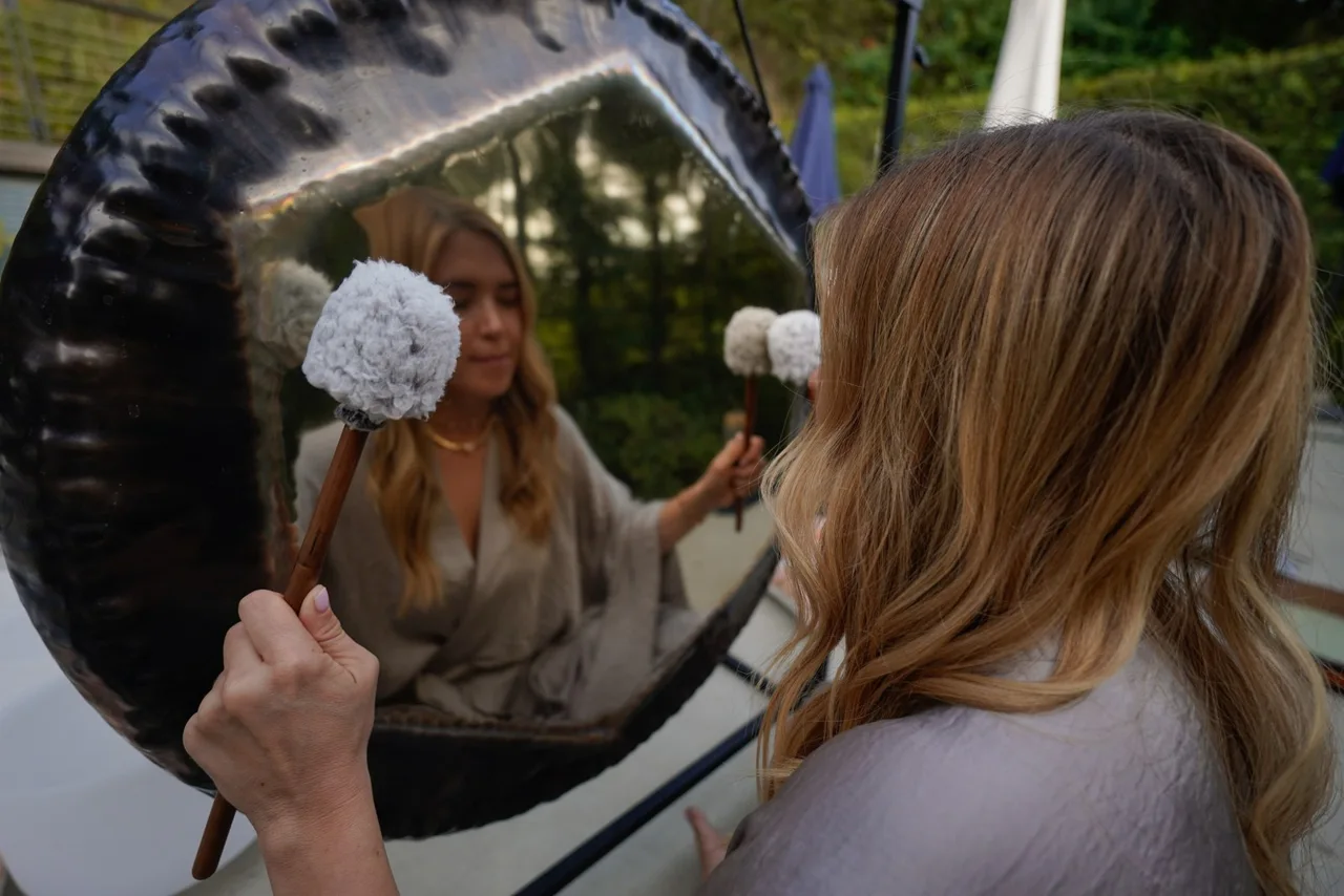 An Om Floating facilitator playing a gong outdoors
